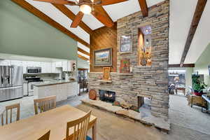 Dining space featuring beamed ceiling, a stone fireplace, sink, and high vaulted ceiling