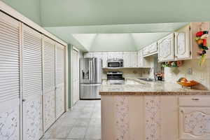 Kitchen with backsplash, sink, light tile patterned floors, kitchen peninsula, and stainless steel appliances