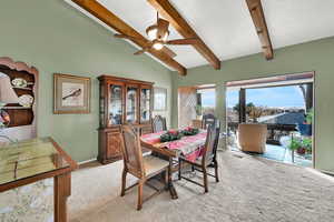 Dining space with ceiling fan, beamed ceiling, high vaulted ceiling, a textured ceiling, and light carpet