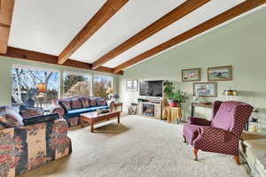 Carpeted living room featuring lofted ceiling with beams