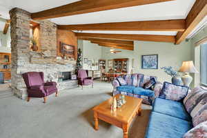 Living room featuring vaulted ceiling with beams, ceiling fan, a stone fireplace, and carpet floors