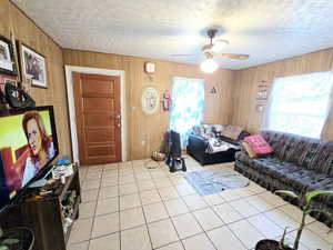 Living room featuring light tile patterned floors, a textured ceiling, ceiling fan, and wooden walls