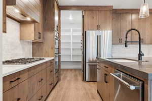 Kitchen featuring dark stone counters, light wood-style floors, custom range hood, appliances with stainless steel finishes, and a sink