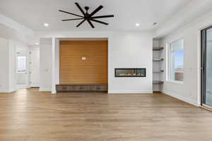 Unfurnished living room with a ceiling fan, visible vents, light wood-style flooring, and a glass covered fireplace