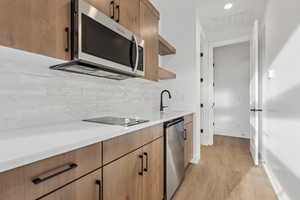 Kitchen featuring decorative backsplash, stainless steel appliances, open shelves, light wood-type flooring, and visible vents