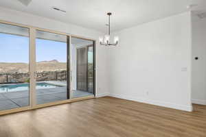 Empty room with wood finished floors, a chandelier, a mountain view, baseboards, and visible vents
