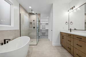 Bathroom with tile patterned flooring, a freestanding bath, vanity, a spacious closet, and a stall shower