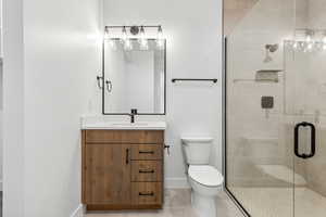 Bathroom featuring vanity, toilet, a stall shower, baseboards, and tile patterned flooring