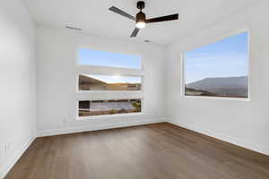 Spare room featuring a ceiling fan, visible vents, wood finished floors, and baseboards