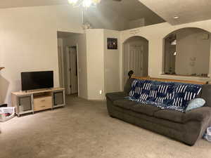 Carpeted living room with ceiling fan and lofted ceiling