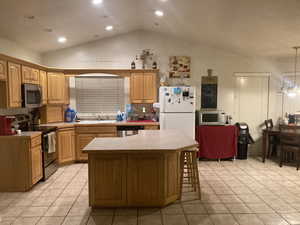 Kitchen with appliances with stainless steel finishes, light tile patterned floors, decorative light fixtures, a kitchen island, and lofted ceiling