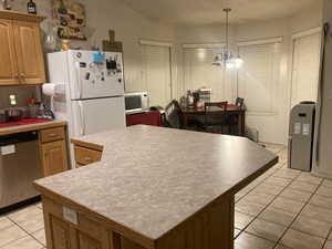 Kitchen featuring white appliances, light tile patterned floors, decorative light fixtures, an inviting chandelier, and a center island