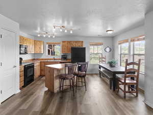 Kitchen featuring black appliances, a center island, wood-type flooring, and a textured ceiling