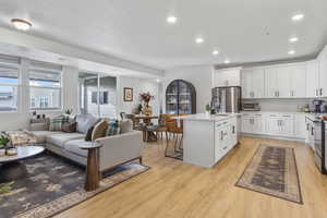 Kitchen with a kitchen breakfast bar, light wood-type flooring, appliances with stainless steel finishes, a kitchen island with sink, and white cabinets