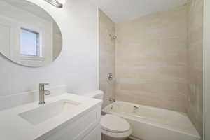 Full bathroom with a textured ceiling, vanity, tiled shower / bath combo, and toilet