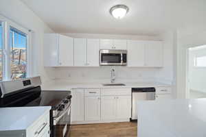 Kitchen with sink, light hardwood / wood-style floors, a textured ceiling, white cabinets, and appliances with stainless steel finishes