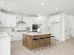 Kitchen with white cabinets, wall chimney exhaust hood, a center island, and light hardwood / wood-style flooring