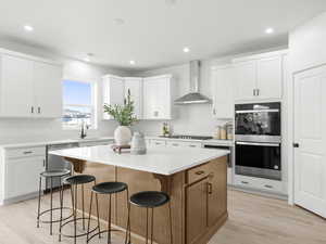 Kitchen featuring a center island, white cabinetry, stainless steel dishwasher, and wall chimney range hood