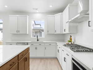 Kitchen featuring light wood-type flooring, wall chimney exhaust hood, stainless steel appliances, sink, and white cabinetry