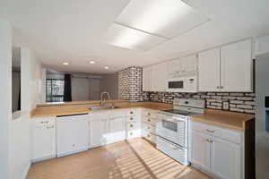 Kitchen featuring sink, backsplash, kitchen peninsula, white appliances, and white cabinets