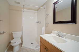 Bathroom featuring toilet, vanity, tiled shower, and tile patterned floors