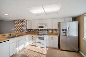 Kitchen featuring tasteful backsplash, white appliances, sink, light hardwood / wood-style floors, and white cabinetry