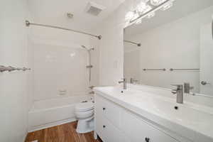 Full bathroom with vanity, tiled shower / bath combo, hardwood / wood-style flooring, and toilet