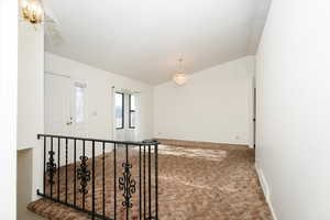 Carpeted empty room with lofted ceiling and an inviting chandelier