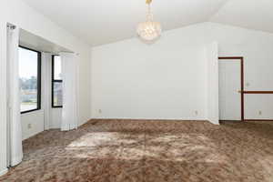 Carpeted empty room with a chandelier and vaulted ceiling