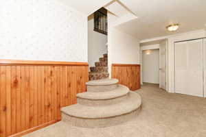 Staircase featuring carpet flooring, ornamental molding, a textured ceiling, and wooden walls