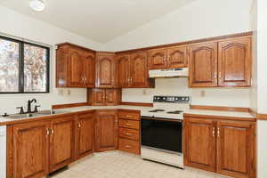 Kitchen with white appliances, vaulted ceiling, and sink