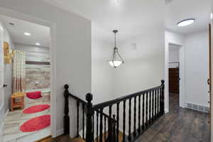 Corridor with dark wood-style floors, stairwell, and chandelier