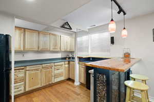 Kitchenette with black fridge, breakfast bar, decorative lighting, and medium-toned hardwood flooring