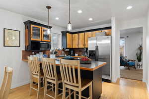 Kitchen with stainless steel appliances, kitchen peninsula, light hardwood floors, a breakfast bar area, and decorative backsplash