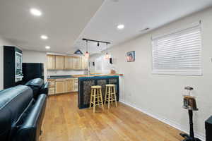 Kitchenette with black fridge, breakfast bar, decorative lighting, and medium-toned hardwood flooring