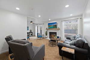 Living room featuring ceiling fan, ornamental molding, a fireplace, and light carpet