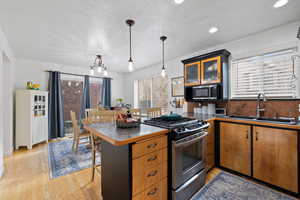 Kitchen featuring sink, stainless steel appliances, kitchen peninsula, pendant lighting, and light hardwood floors