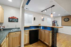 Kitchenette with black fridge, breakfast bar, decorative lighting, and medium-toned hardwood flooring