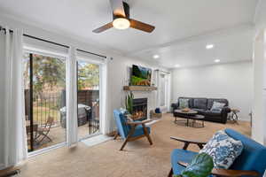 Living room featuring carpet, ceiling fan, and crown molding, fireplace, and sliding glass door to back patio