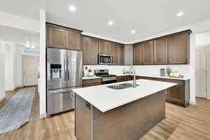 Kitchen with sink, an island with sink, light hardwood / wood-style floors, dark brown cabinetry, and stainless steel appliances