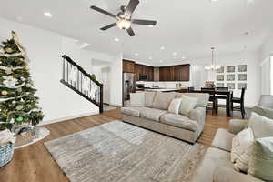 Living room with ceiling fan with notable chandelier and light hardwood / wood-style floors