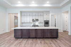 Kitchen with white cabinets, light hardwood / wood-style floors, double oven, and a large island