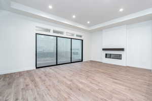 Unfurnished living room with a large fireplace, light hardwood / wood-style floors, and a tray ceiling