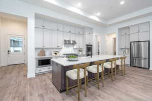 Kitchen with a kitchen bar, light wood-type flooring, stainless steel appliances, and a center island with sink