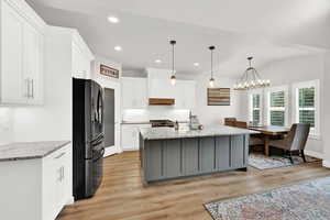 Kitchen featuring black fridge, an island with sink, light hardwood / wood-style floors, decorative light fixtures, and white cabinets