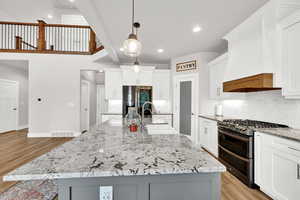 Kitchen featuring a center island with sink, range with two ovens, stainless steel refrigerator with ice dispenser, light hardwood / wood-style flooring, and decorative light fixtures