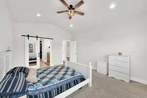 Bedroom with ensuite bath, vaulted ceiling, ceiling fan, a barn door, and light colored carpet