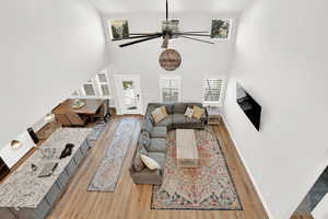 Living room with ceiling fan, a high ceiling, and light hardwood / wood-style flooring