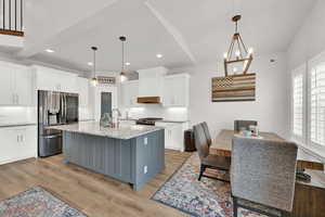 Kitchen with premium range hood, a kitchen island with sink, white cabinetry, and stainless steel appliances