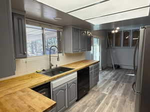 Kitchen featuring butcher block counters, light wood-style floors, freestanding refrigerator, a sink, and dishwasher